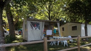 A campsite with a covered area, a small building, and a fenced area with chairs and tables. - Le Camping St Etienne (Villefranche-de-Panat)