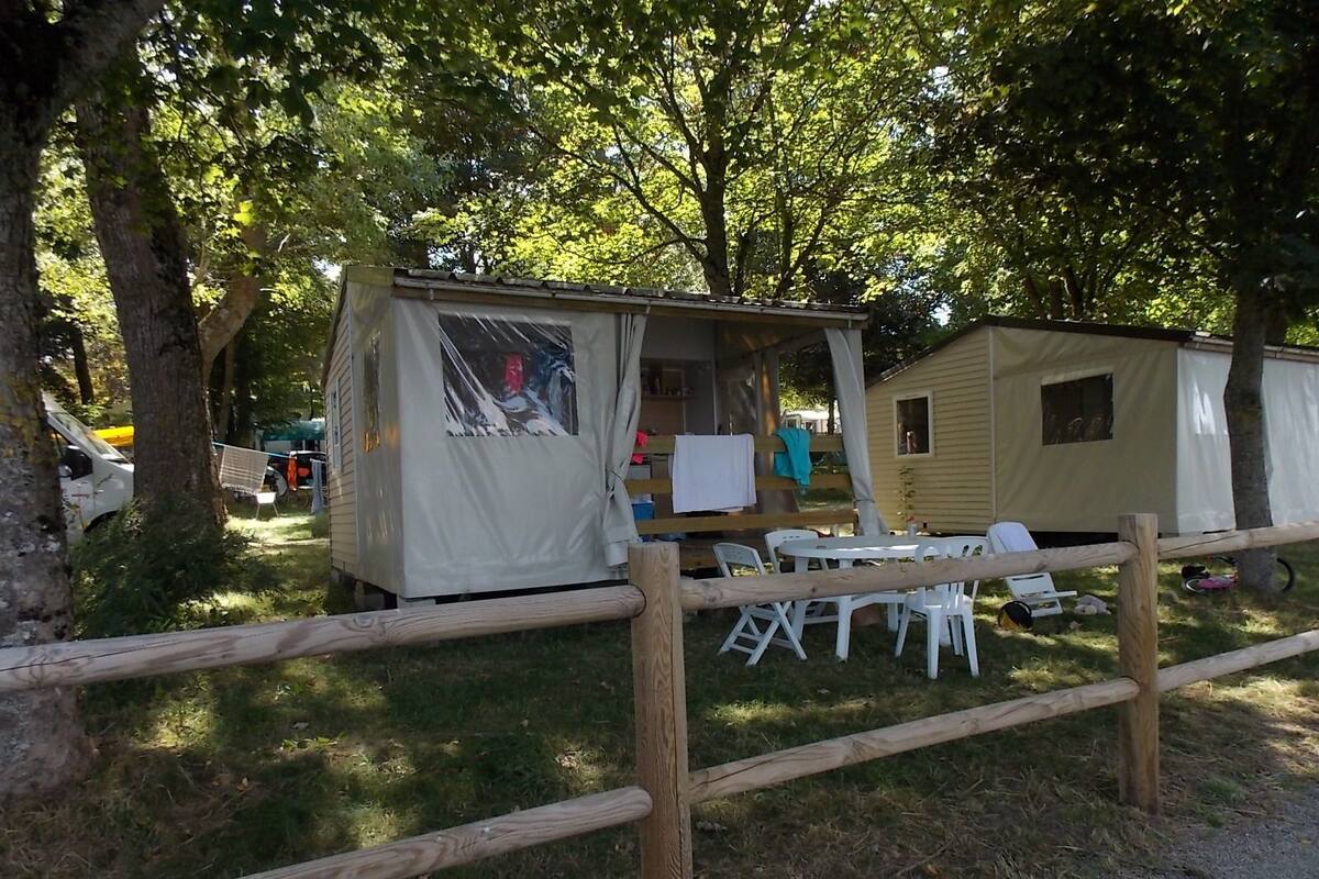 A campsite with a covered area, a small building, and a fenced area with chairs and tables.