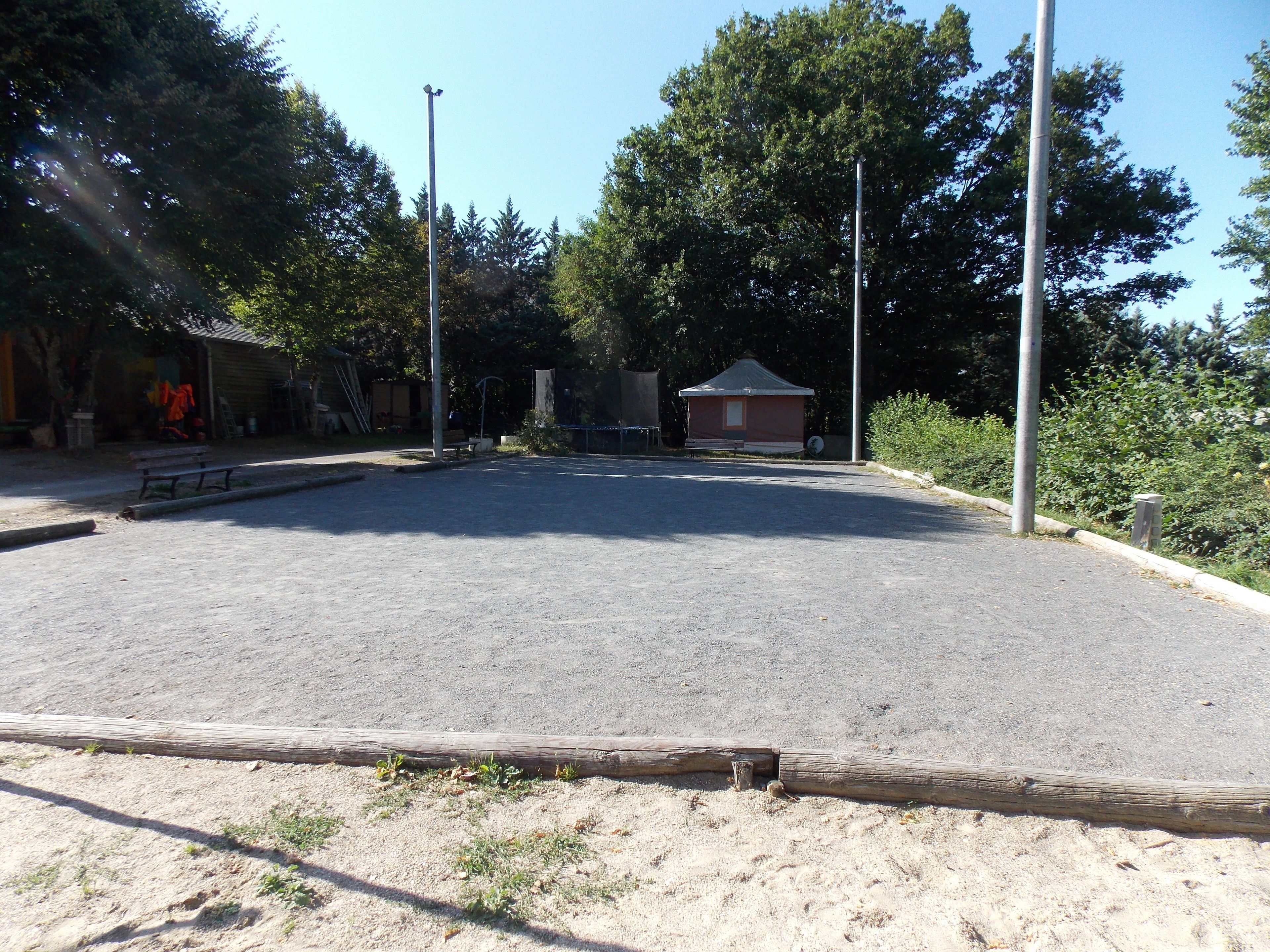 Un espacio al aire libre con suelo pavimentado, rodeado de árboles y un pequeño edificio.