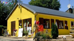 A yellow building with a sloped roof, a satellite dish, and a small garden area with potted plants and a stone wall. - Le Camping St Etienne (Villefranche-de-Panat)