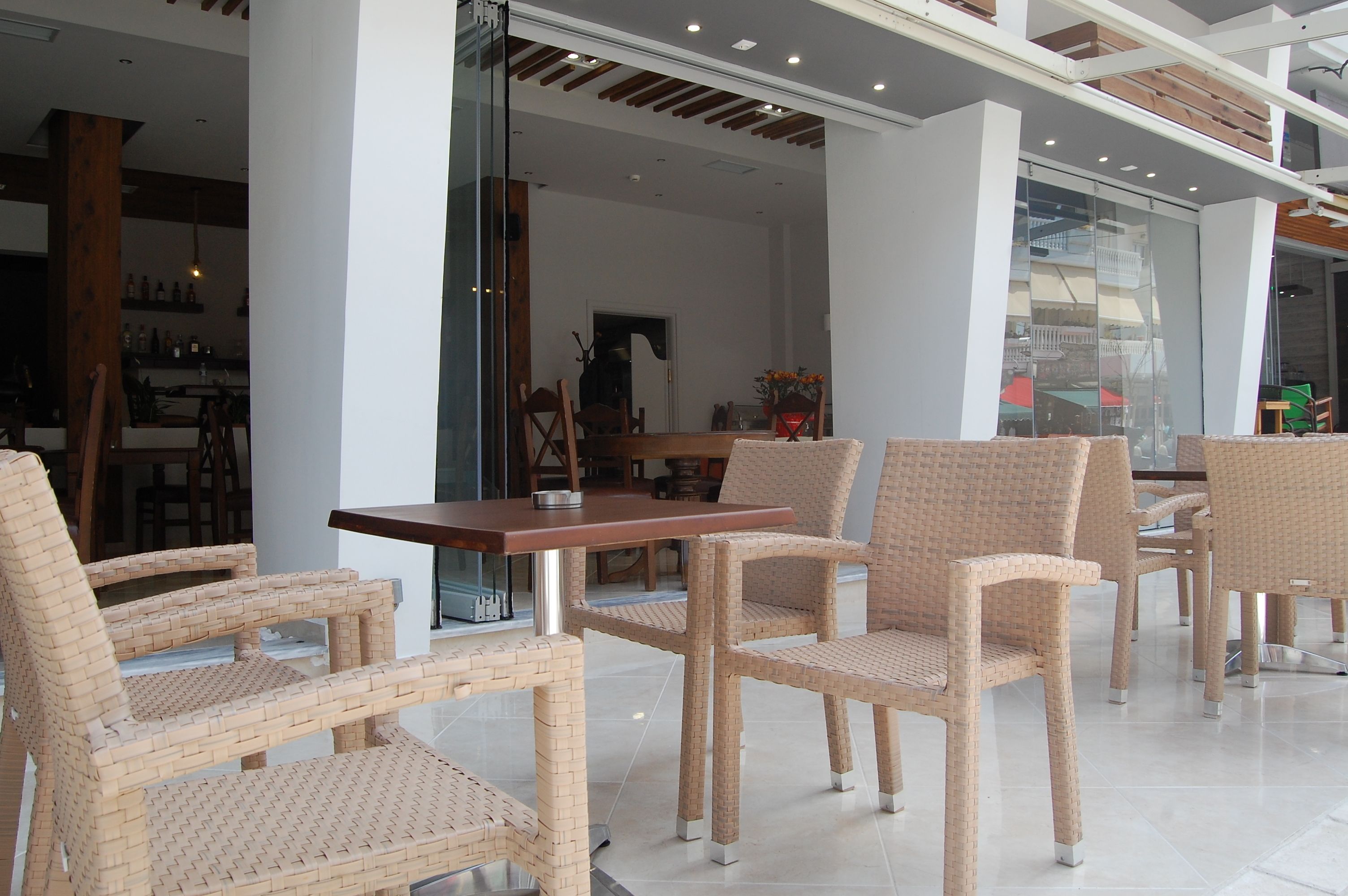 A modern indoor seating area with wicker chairs and a wooden table, featuring a glass partition and a view of the interior.