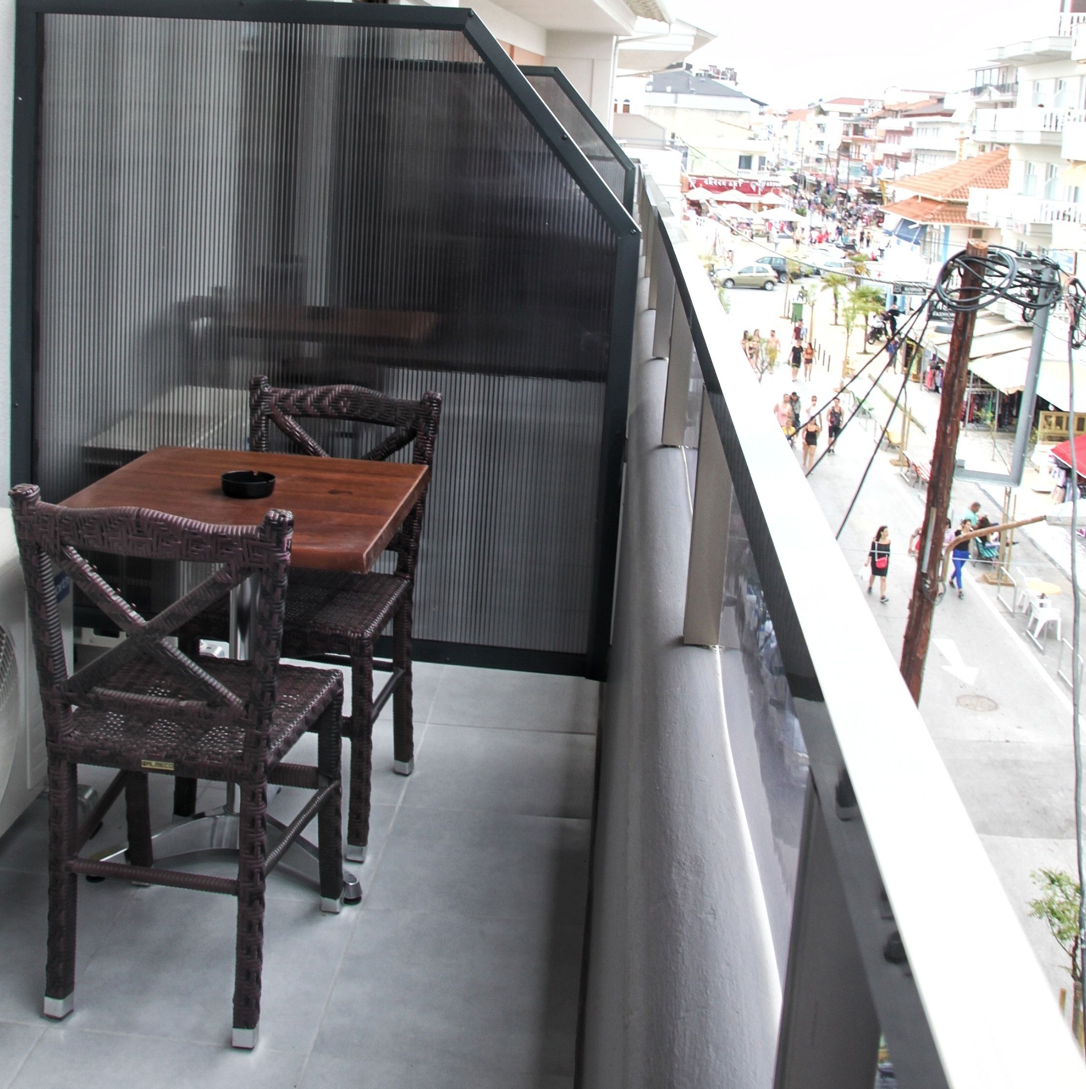 A balcony with a wooden table and chairs, a view of a busy street below.