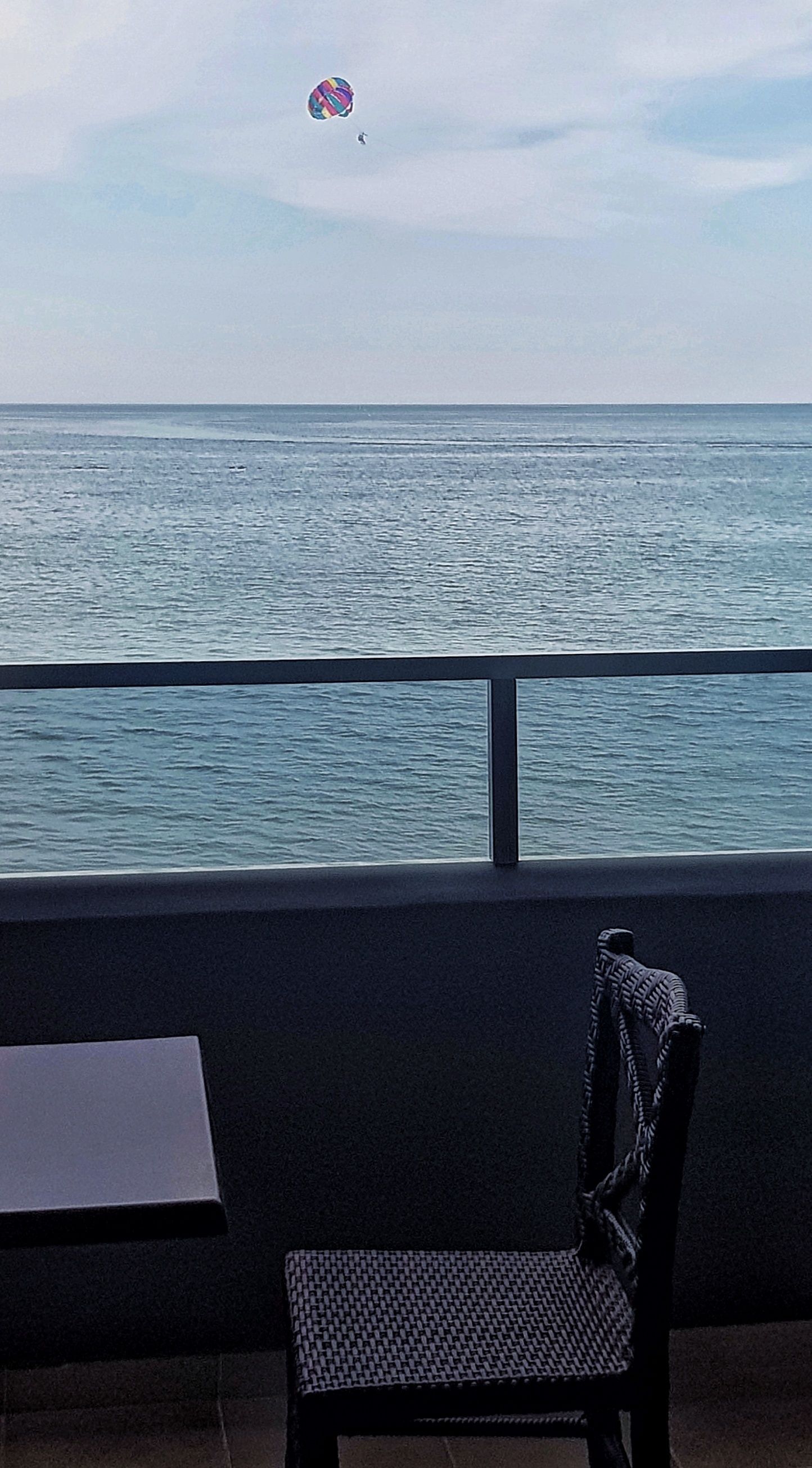 A chair facing a balcony with a view of the sea.