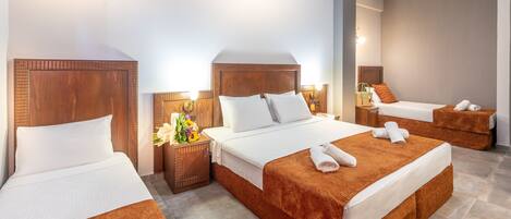 A hotel room with three beds, a wooden headboard, a nightstand with a lamp, and a wall-mounted light fixture.