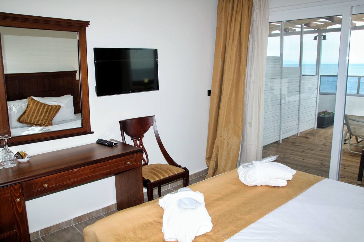 A hotel room with a bed, a desk, a chair, a TV, and a view of the sea.