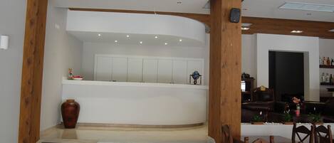 A reception area with a curved counter, wooden beams, a vase, and a staircase leading to a dining area with chairs and a table.