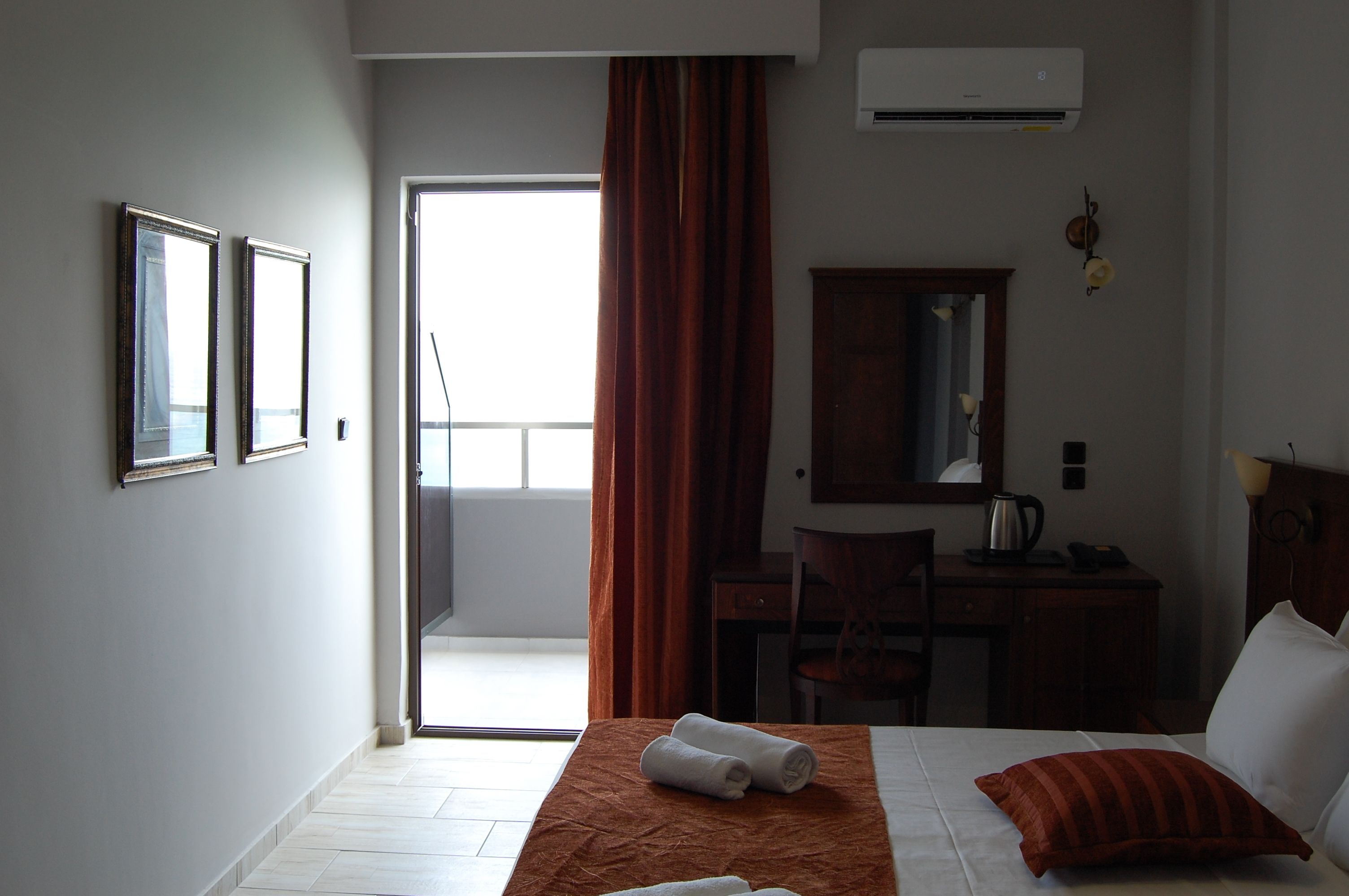 Una habitación de hotel con cama, escritorio, silla, espejo y aire acondicionado.