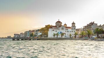 Un pueblo costero con una iglesia blanca destacada con cúpulas, un muelle que se extiende hacia el mar y edificios con balcones.