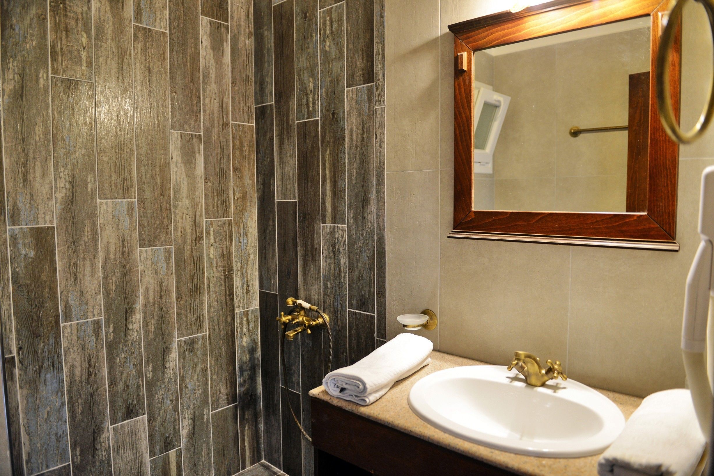 Un baño con pared de ducha de madera, un lavamanos con grifo dorado y un espejo con marco de madera.