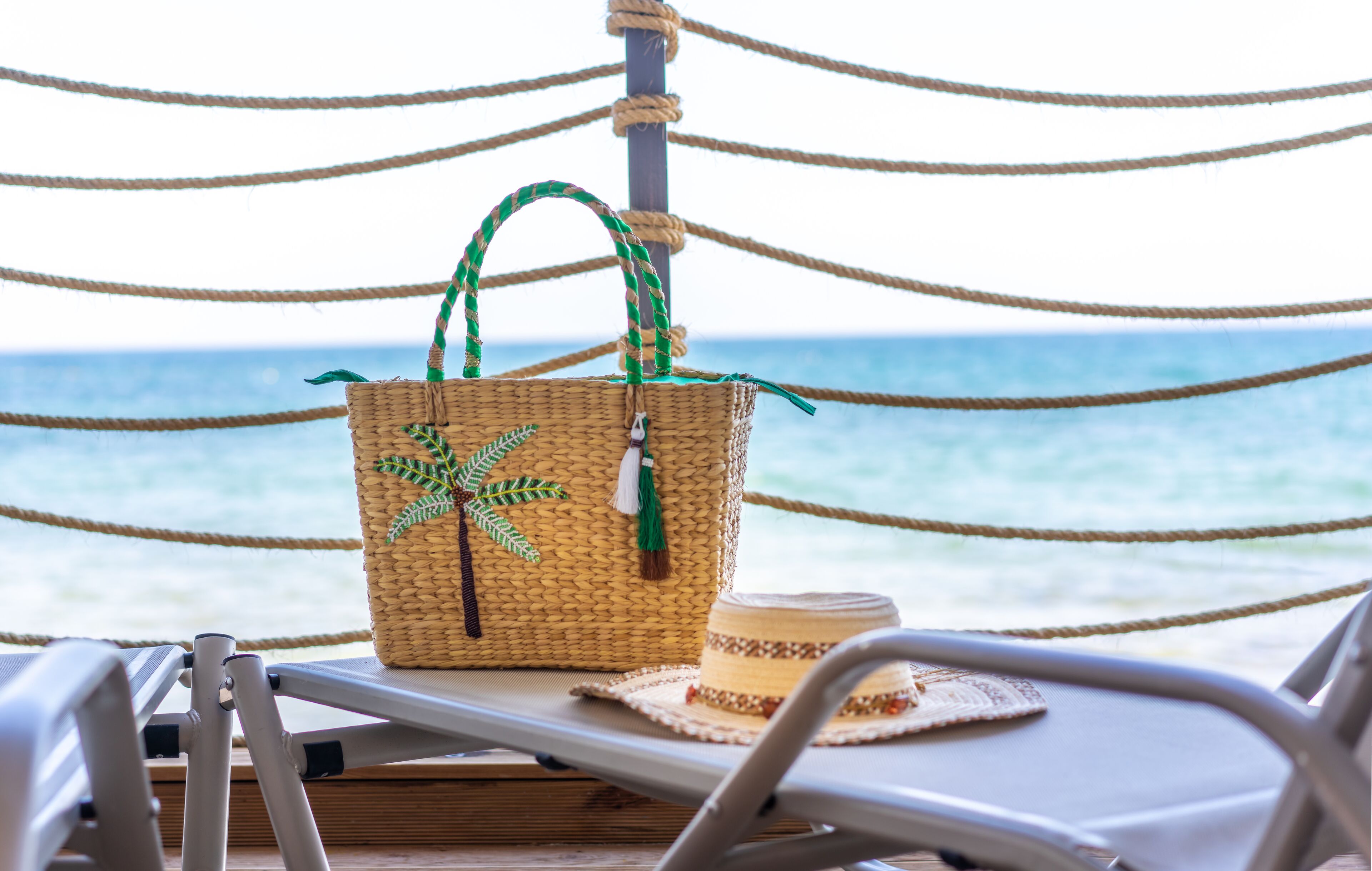 A wicker basket with a green handle and a straw hat on a deck chair.