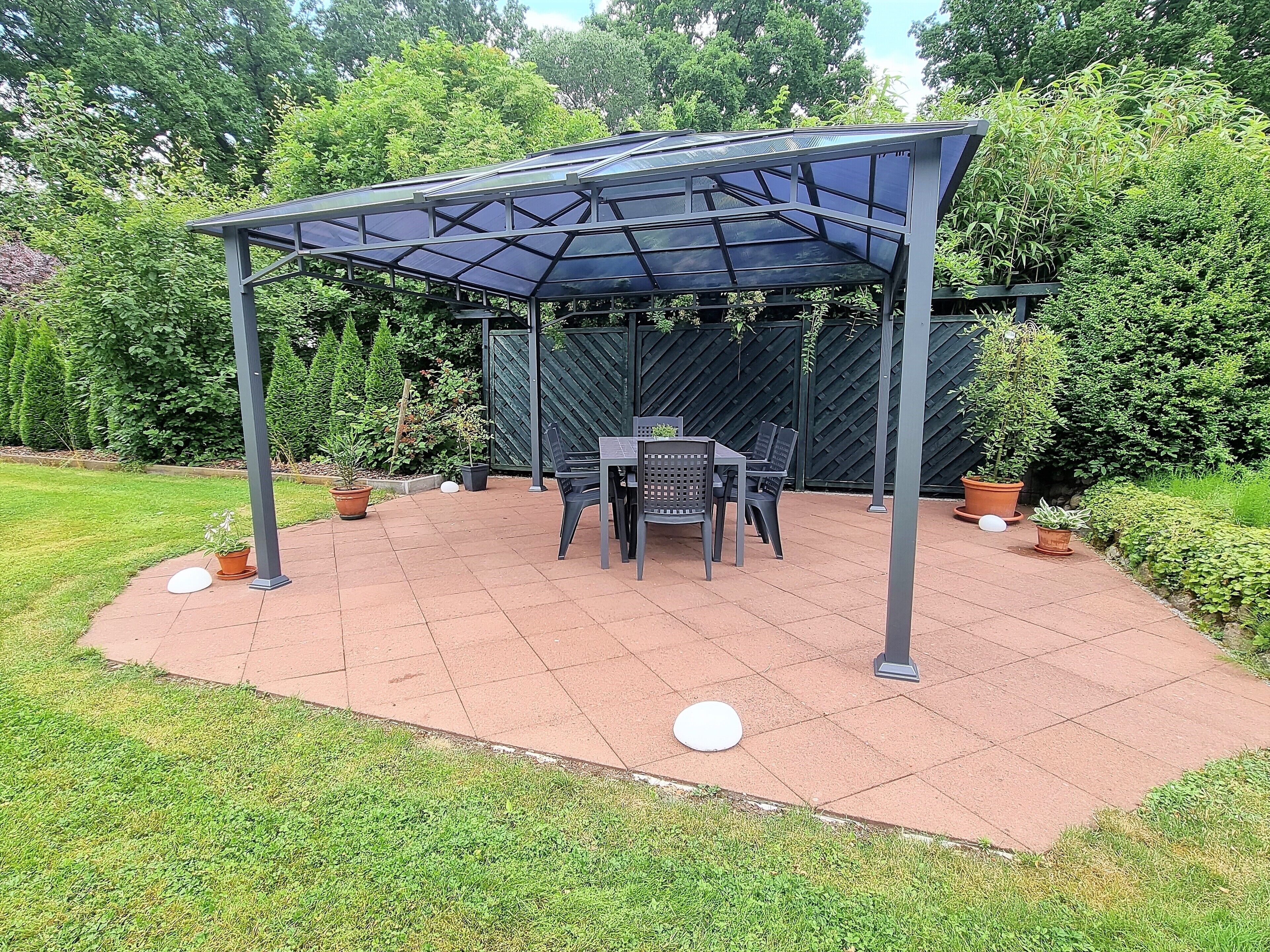 Un patio couvert, aménagé avec une table et des chaises, entouré de plantes en pot et d’une clôture.