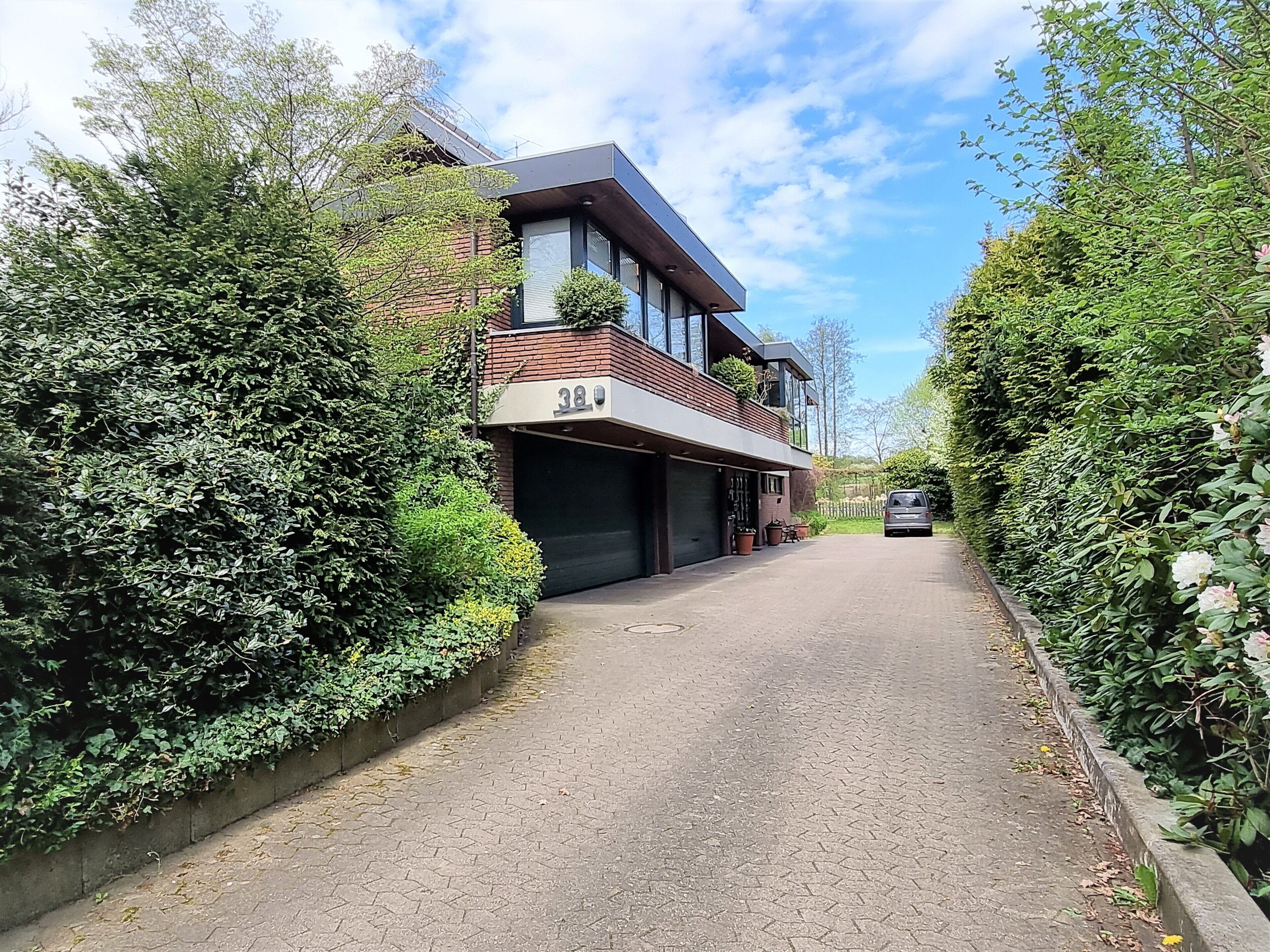 Ein modernes, zweistöckiges Haus mit Garage, umgeben von üppigem Grün und blauem Himmel.