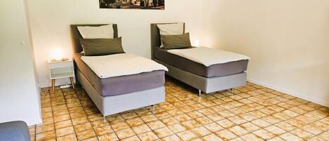 A small, clean room with two single beds, a nightstand, and a wall-mounted picture.