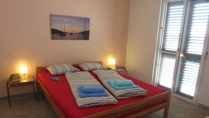 Une chambre à coucher avec un lit en bois, une literie rouge, deux tables de chevet avec des lampes et une fenêtre avec des stores.