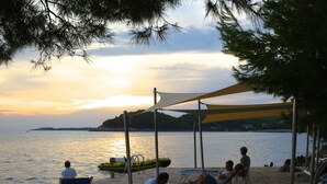 Une plage avec un sol pavé de pierres, un kayak jaune et des personnes se détendant à l’ombre.