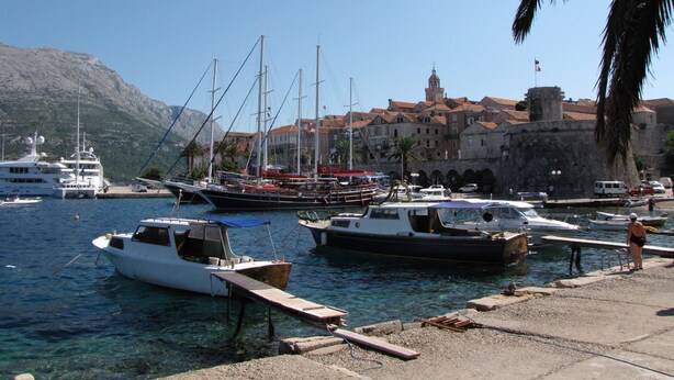 Un port de plaisance où sont amarrés différents types de bateaux, un bâtiment historique doté d’une tour et une eau d’un bleu cristallin.