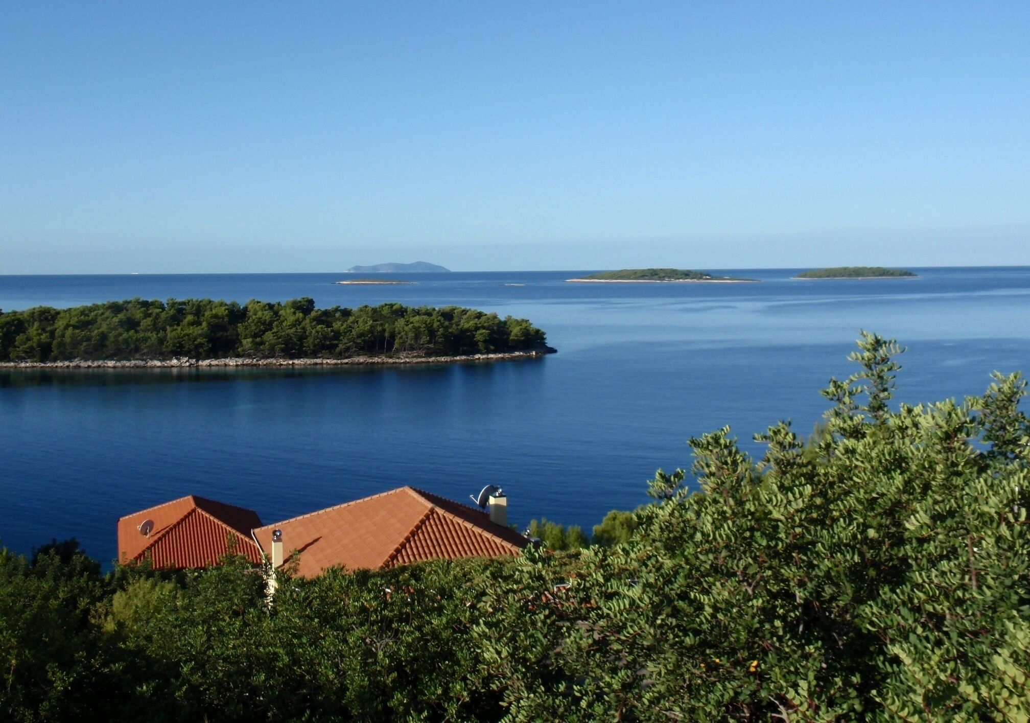 A coastal landscape with a clear view of the sea, a small island, and a building with a red roof in the foreground.