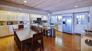 A spacious kitchen with wooden flooring, white cabinetry, a central island, and stainless steel appliances. - Luxury Ocean Front Home (Aptos)