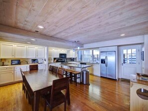Uma cozinha espaçosa com piso de madeira, armários brancos, uma ilha central e eletrodomésticos de aço inoxidável.