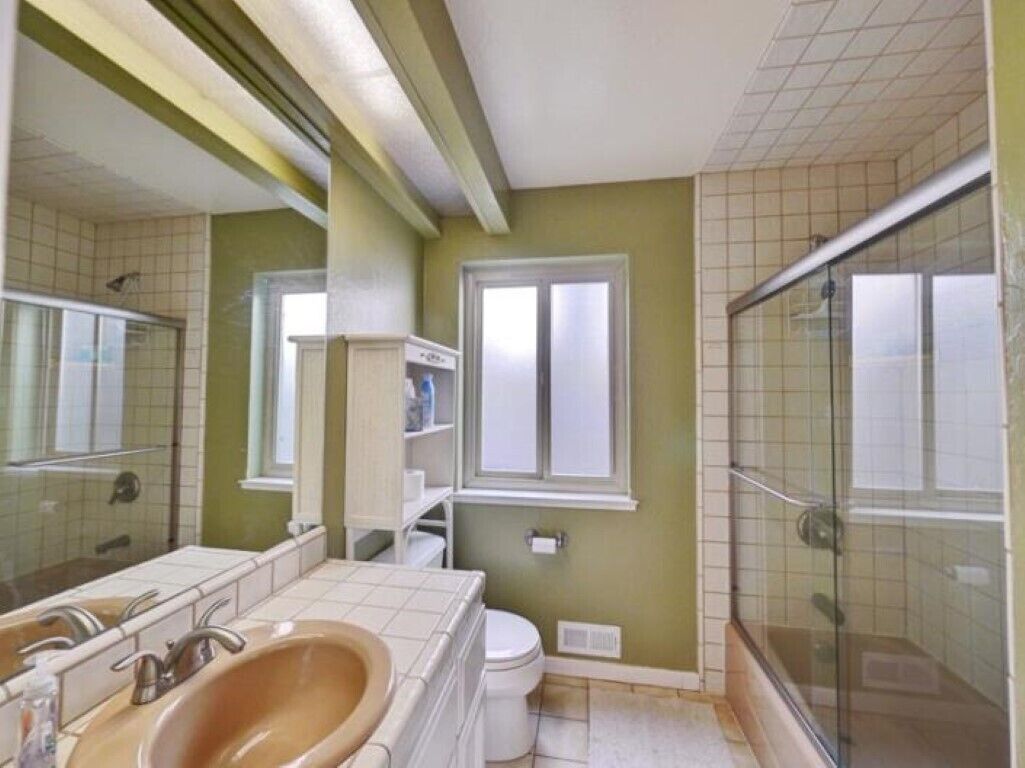 A bathroom with a double sink, toilet, and a glass-enclosed shower area.