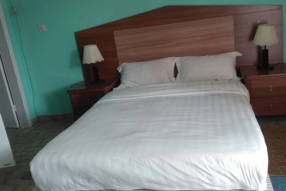 A neatly made bed with white linens, a wooden headboard, two bedside tables with lamps, and a patterned rug on the floor.