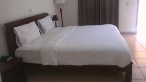 En snyggt bäddad säng i ett hotellrum med en sänggavel i trä, en sänglampa och ett fönster med gardiner.