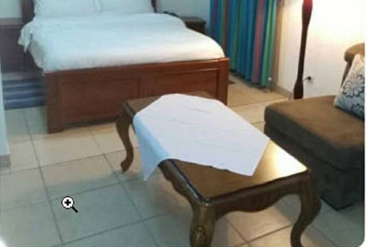 A hotel room with a wooden bed, a small table with a white cloth, a sofa, and a striped curtain.