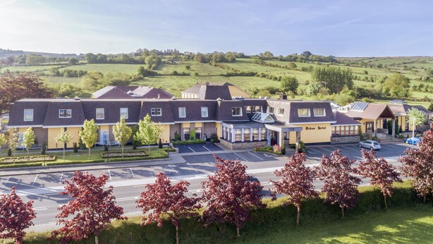 A hotel with multiple buildings, a parking lot, and a green landscape in the background.
