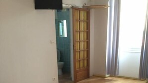 A bedroom with a bed, a television mounted on the wall, and a wooden door leading to a bathroom. - Auberge de Saint Rome (Saint-Rome-de-Tarn)