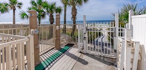 A gated entrance to a beach area with palm trees and a view of the ocean.