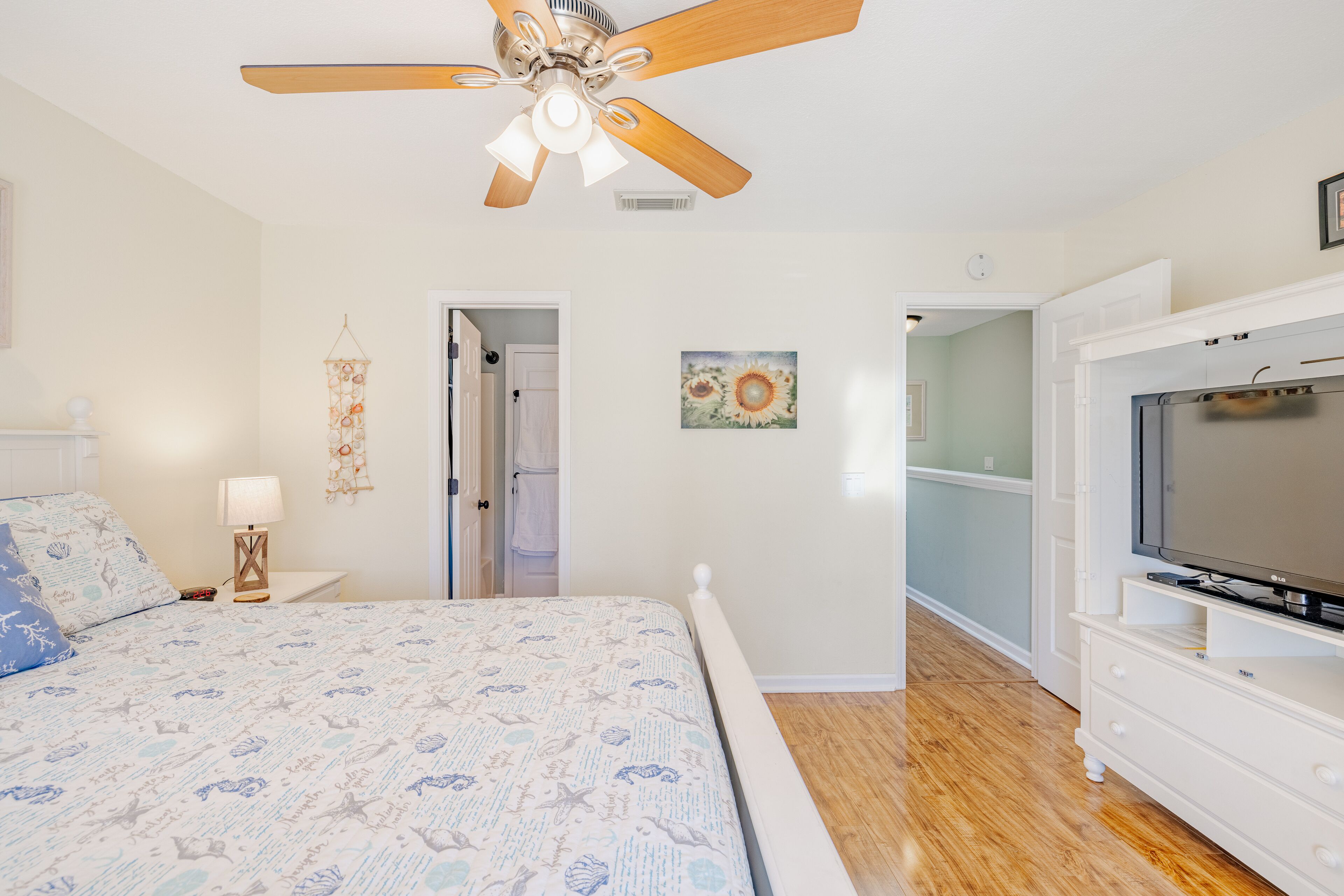 A bedroom with a bed, a ceiling fan, a TV, and a door leading to another room.