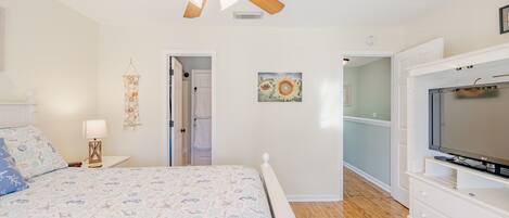 A bedroom with a bed, a ceiling fan, a TV, and a door leading to another room.