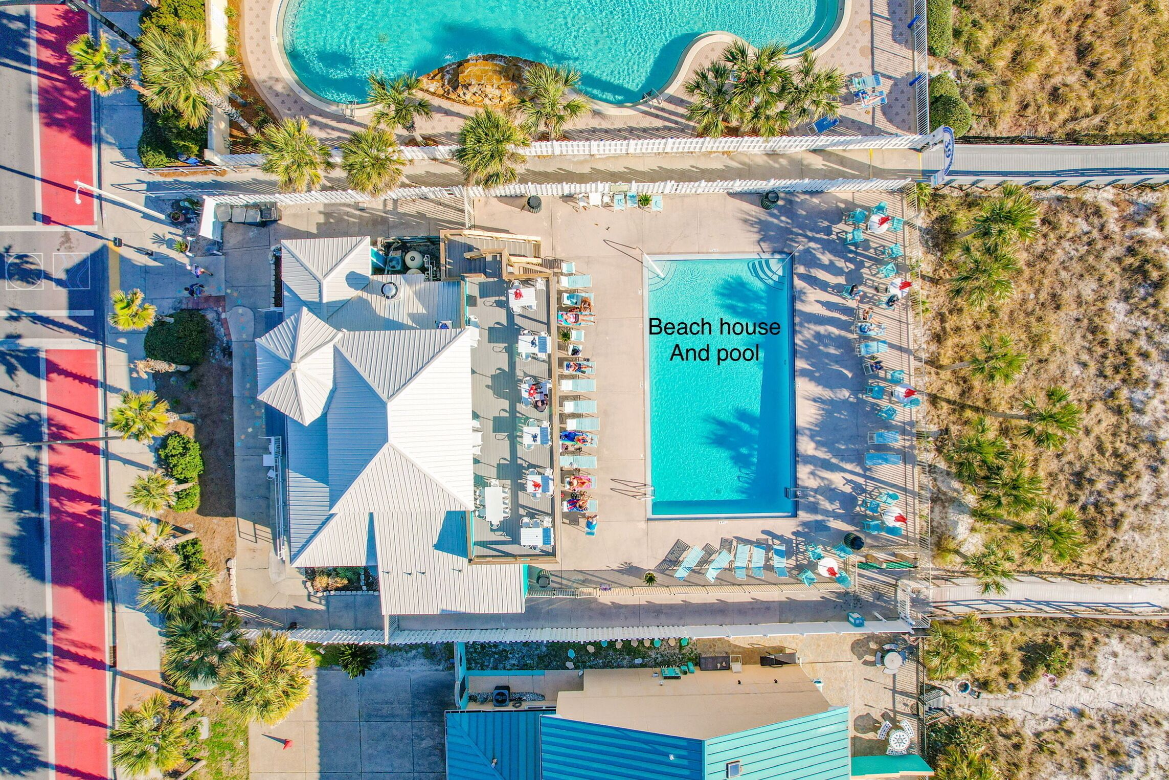 Vista aerea di una casa sulla spiaggia con piscina, con area solarium, poltrone a sdraio e ombrelloni, circondata da palme e acqua cristallina.