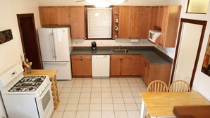 A compact kitchen with wooden cabinets, a white refrigerator, a microwave, a dishwasher, a stove, and a dining table with chairs. - Spacious 1br Apartment in Raritan- Fully Furnished!  (Raritan)