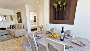 Un coin repas avec une table dressée pour deux personnes, agrémenté d’une bouteille de vin, d’assiettes et d’une feuille décorative.