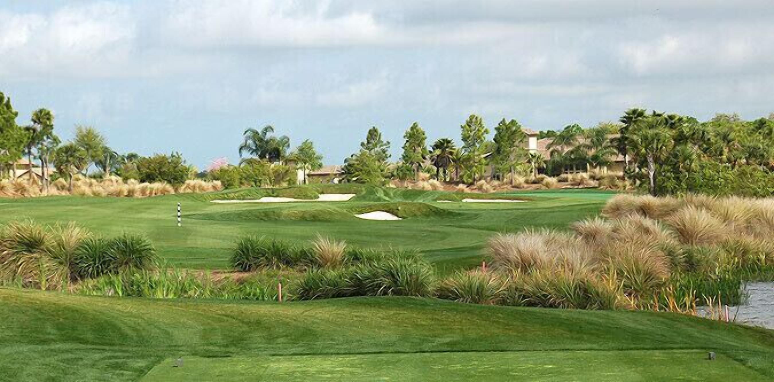 A golf course with sand bunkers, water hazards, and a clubhouse in the background.