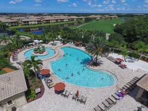 Ein Resort mit einem großen, zentral gelegenen Swimmingpool, umgeben von Liegebereichen und Palmen.