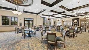 Un vaste espace dédié à la salle à manger, avec de nombreuses tables et chaises, de grandes fenêtres et un tapis à motifs.