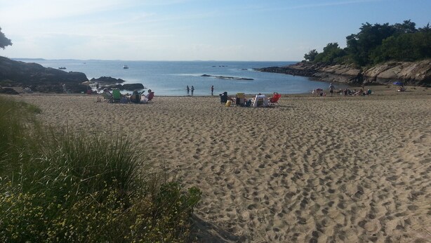 Une plage de sable où l’on voit des gens et des bateaux dans l’eau.