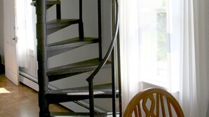 Un escalier en colimaçon dans une pièce dotée d’un plancher en bois, d’une porte blanche et d’une fenêtre ornée de rideaux blancs.