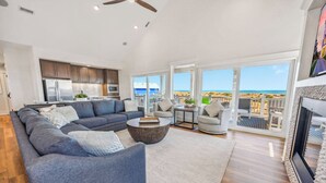Ett rymligt vardagsrum med en grå soffa, ett soffbord och utsikt över stranden genom stora fönster.