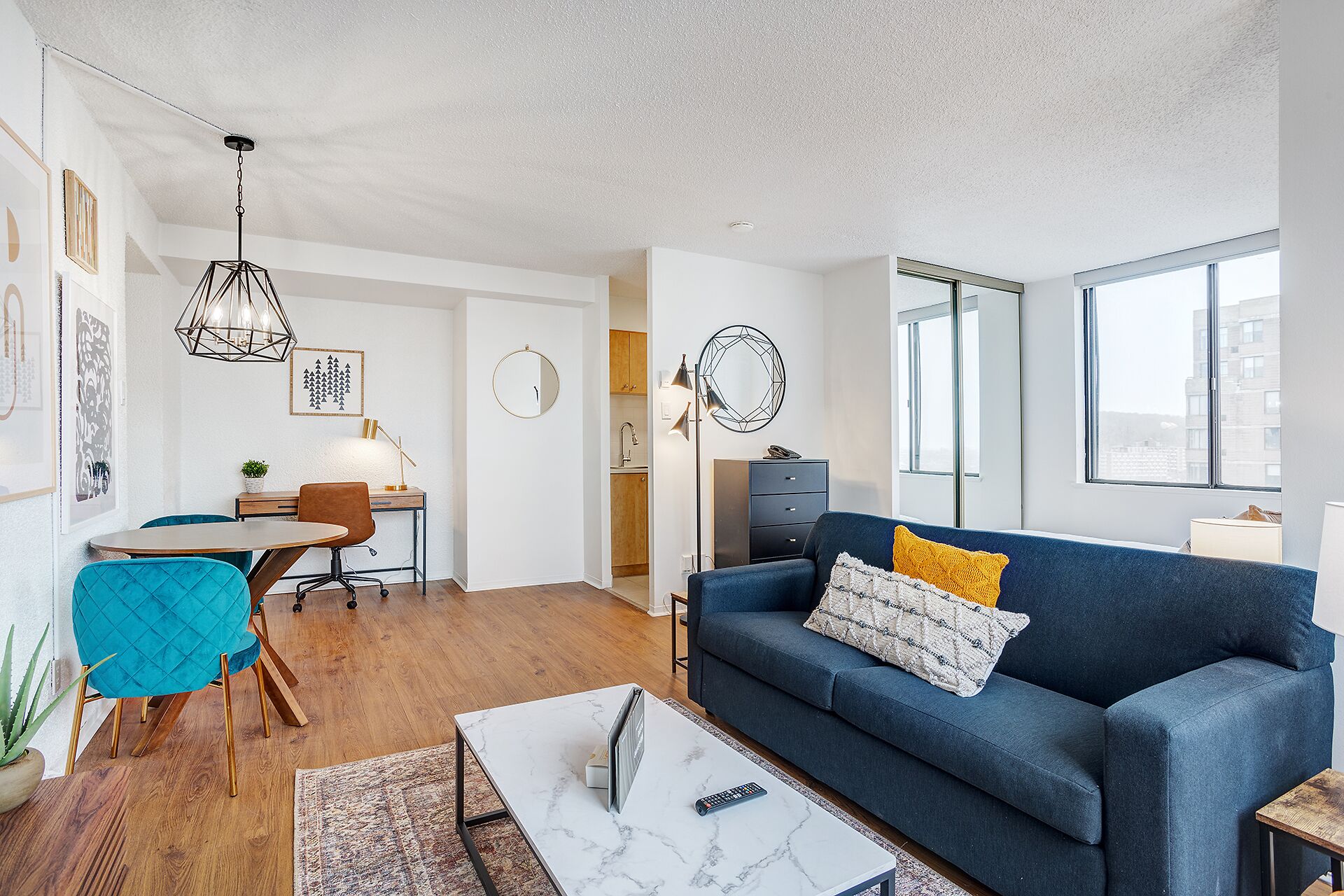 Una sala de estar moderna con un sofá azul, una zona de comedor con una mesa y sillas de madera, y una cocina al fondo.