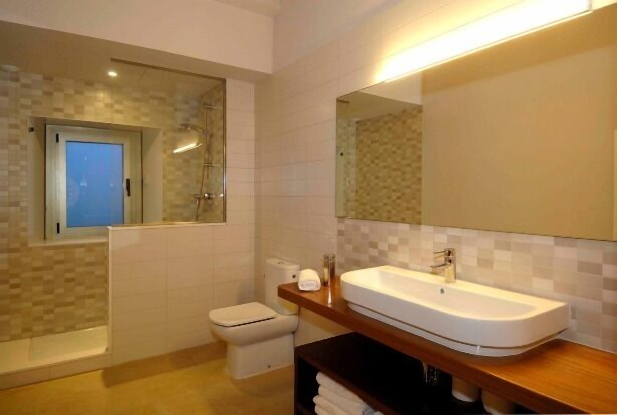 Une salle de bain moderne avec un grand miroir, un lavabo blanc et une douche à parois de verre.