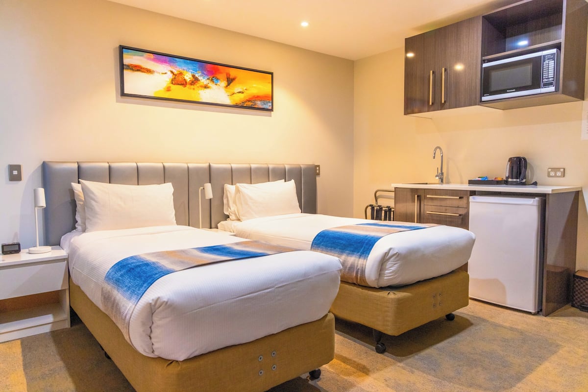 A hotel room with two beds, a small kitchenette, a microwave, and a painting on the wall.