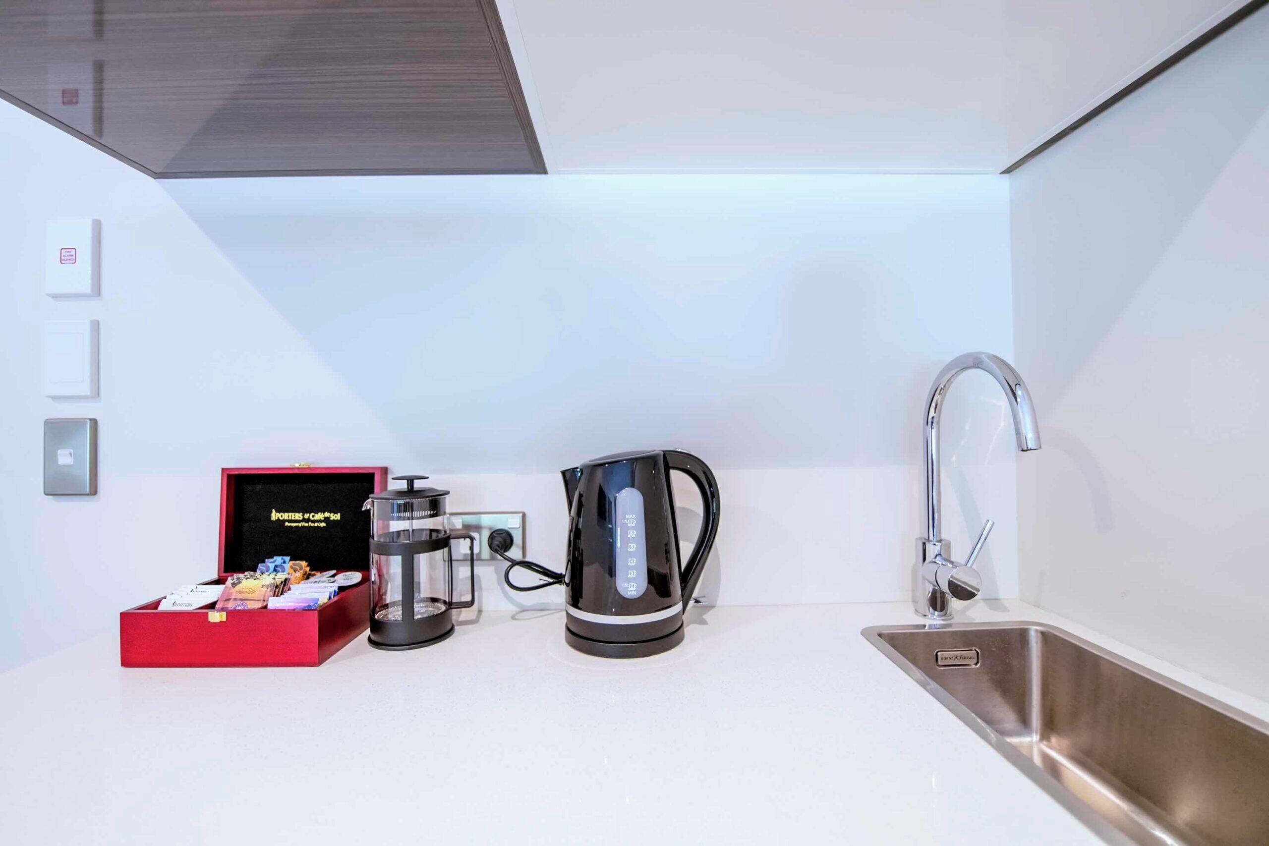 Een moderne keuken met een koffiezetapparaat, een waterkoker en een rode doos koffiecups.