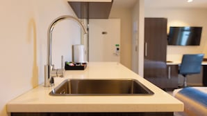 A modern kitchen with a stainless steel sink, a built-in oven, and a flat-screen TV mounted on the wall. - Alpine Hotel (Christchurch)