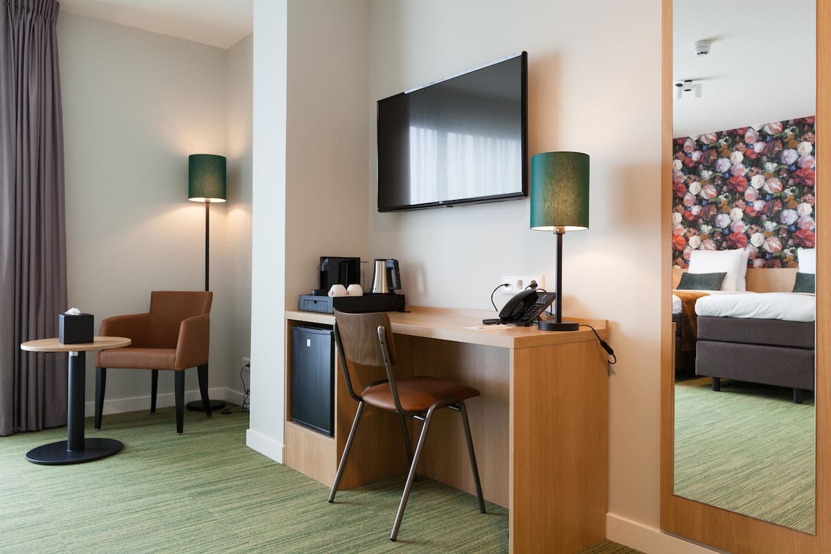 Una camera d'albergo con una scrivania, una sedia, una televisione e un letto con carta da parati a motivi floreali.