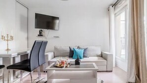 Ein modernes Wohnzimmer mit einem weißen Sofa, zwei schwarzen Sesseln, einem Couchtisch und einem an der Wand befestigten Flachbildfernseher.