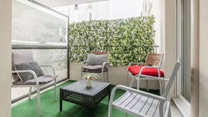Ein Balkon mit künstlichem Rasen, weißen Metallstühlen, einem kleinen Tisch mit einer Vase und einer Hecke als Wand.