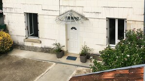 Un edificio de dos pisos con fachada blanca, techo gris y un pequeño porche con sombrilla metálica.